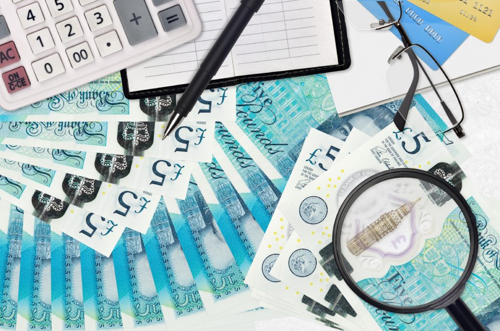 5 British pounds bills and calculator with glasses and pen. Tax payment season concept or investment solutions. Searching a job with high salary